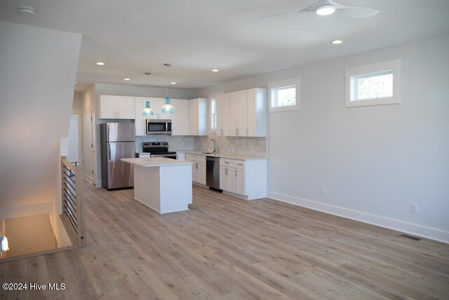 kitchen with white cabinets, a kitchen island, decorative light fixtures, and appliances with stainless steel finishes