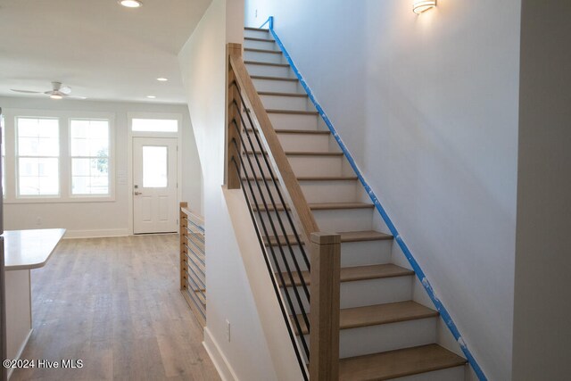 staircase with hardwood / wood-style floors and ceiling fan