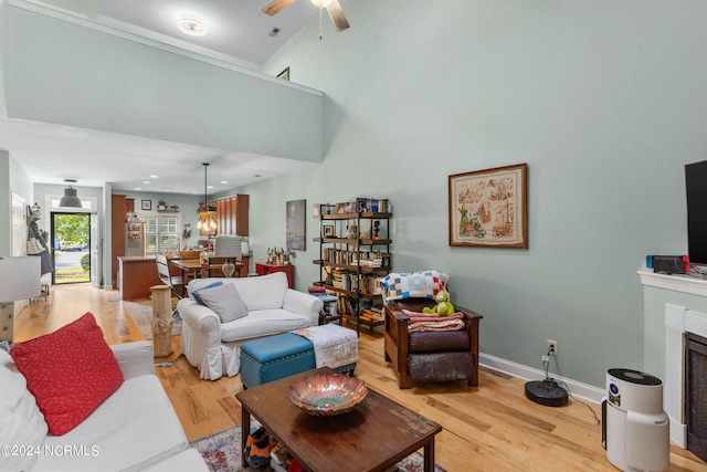 living room with light hardwood / wood-style flooring, a towering ceiling, and ceiling fan with notable chandelier