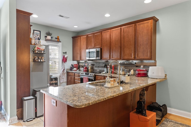 kitchen with light stone countertops, sink, stainless steel appliances, backsplash, and kitchen peninsula