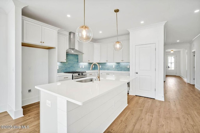 kitchen with light wood-type flooring, a sink, gas stove, wall chimney range hood, and decorative backsplash