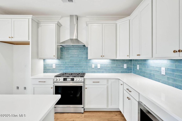 kitchen with gas stove, white cabinetry, light countertops, and wall chimney range hood