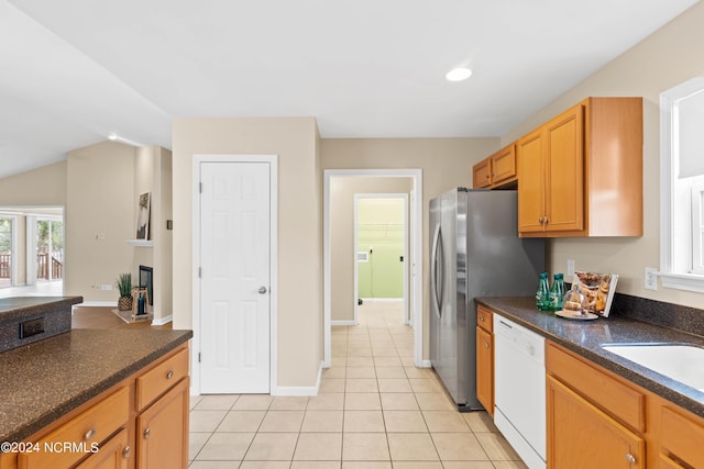 kitchen with a glass covered fireplace, dark countertops, white dishwasher, a sink, and light tile patterned floors
