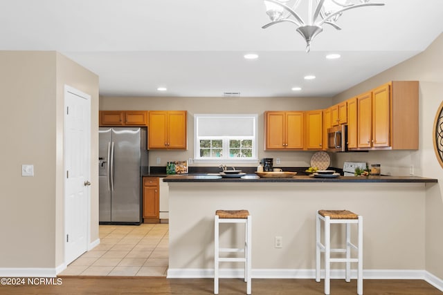 kitchen with a kitchen breakfast bar, kitchen peninsula, appliances with stainless steel finishes, and light hardwood / wood-style flooring