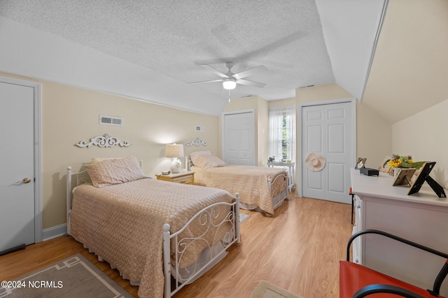 bedroom with light wood-type flooring, a textured ceiling, vaulted ceiling, and ceiling fan