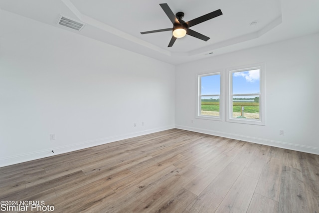 unfurnished room with a raised ceiling, ceiling fan, and light hardwood / wood-style flooring