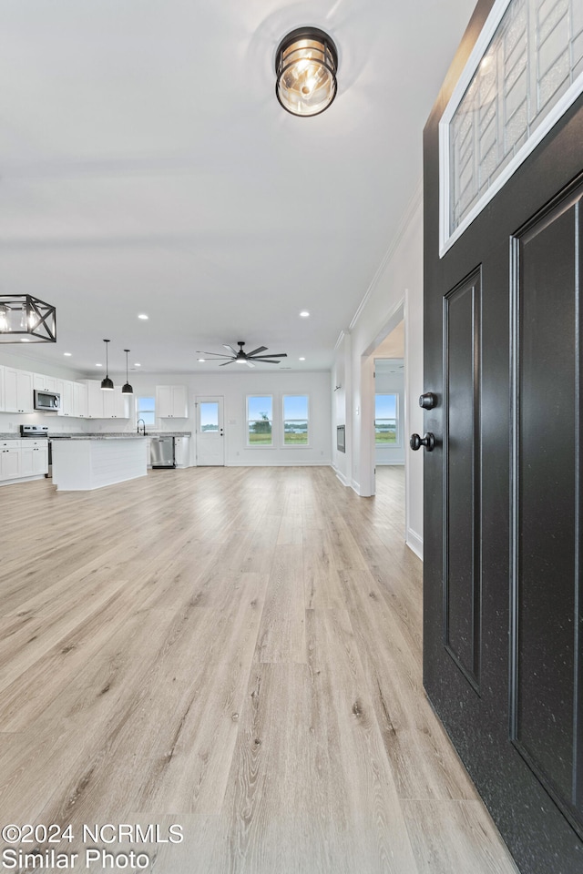 foyer entrance with ceiling fan, light wood-type flooring, and crown molding