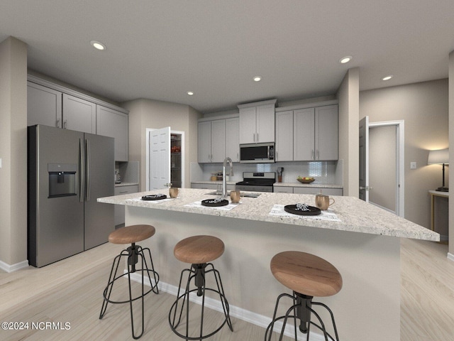 kitchen featuring a center island with sink, appliances with stainless steel finishes, a breakfast bar, gray cabinetry, and light hardwood / wood-style floors