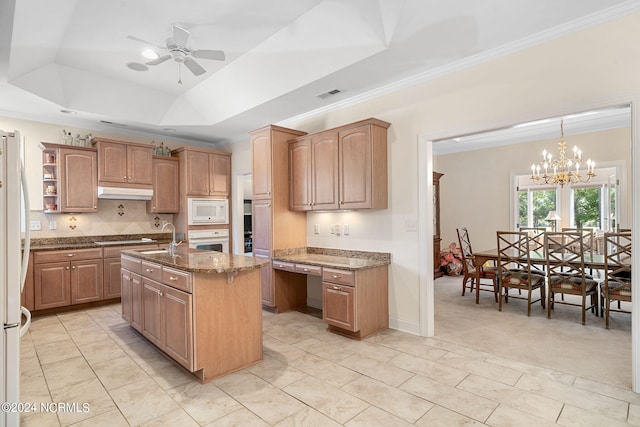 kitchen with an island with sink, pendant lighting, light colored carpet, white appliances, and a tray ceiling