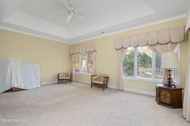 sitting room with ceiling fan, a raised ceiling, light colored carpet, and ornamental molding