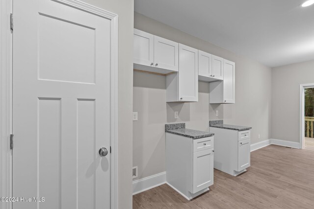 kitchen with light hardwood / wood-style flooring, white cabinetry, and dark stone counters