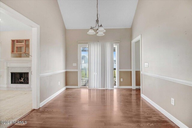 unfurnished dining area with a chandelier, hardwood / wood-style flooring, a fireplace, and lofted ceiling