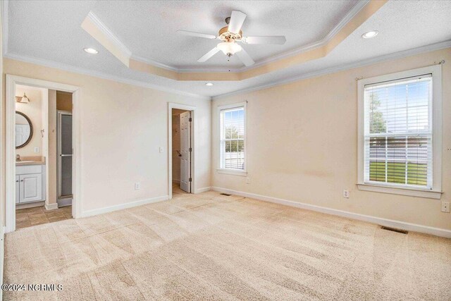 unfurnished bedroom with a tray ceiling, ensuite bath, a spacious closet, and ornamental molding