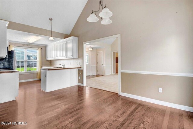 kitchen with kitchen peninsula, vaulted ceiling, hardwood / wood-style flooring, white cabinetry, and hanging light fixtures