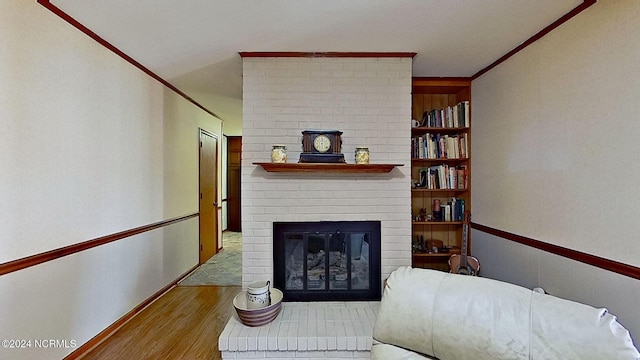 living room featuring light hardwood / wood-style flooring, built in shelves, a brick fireplace, and crown molding