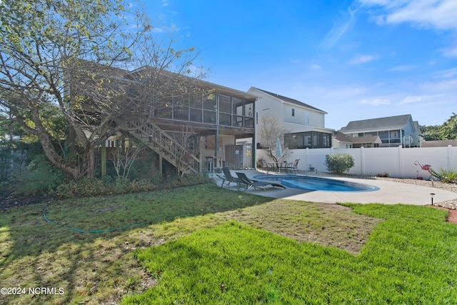 rear view of house with a fenced in pool, a sunroom, a lawn, and a patio