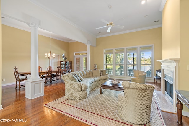 living room featuring a premium fireplace, ornamental molding, wood-type flooring, and ceiling fan with notable chandelier