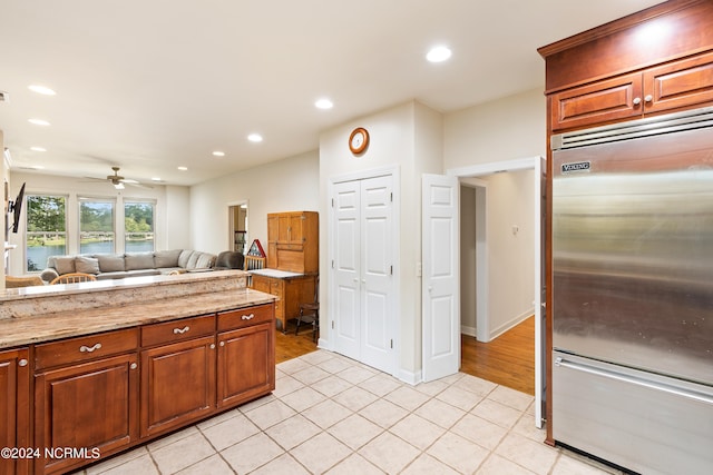 kitchen featuring stainless steel built in fridge, light stone counters, light tile patterned flooring, and ceiling fan