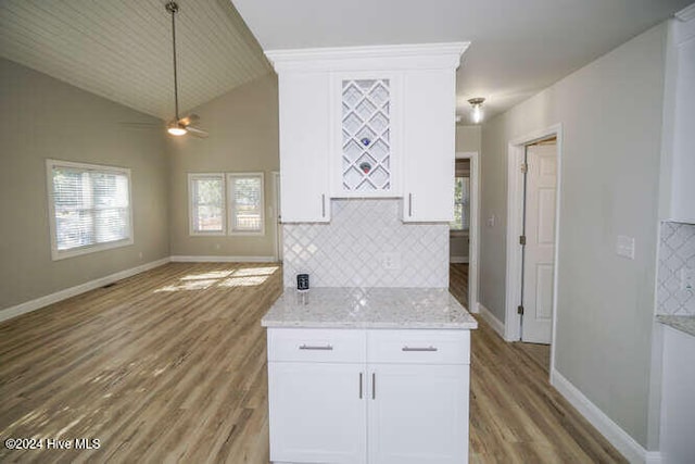 kitchen with light stone counters, backsplash, open floor plan, white cabinetry, and wood finished floors