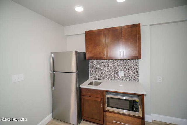 kitchen with stainless steel appliances, a sink, baseboards, light countertops, and tasteful backsplash