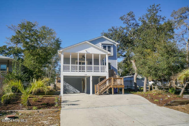 coastal home with concrete driveway, covered porch, stairway, a ceiling fan, and a carport