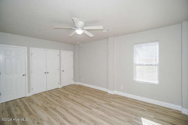 unfurnished bedroom featuring light wood-style floors, ceiling fan, baseboards, and multiple closets