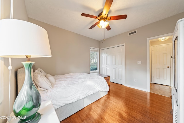 bedroom with baseboards, visible vents, a ceiling fan, wood finished floors, and a closet