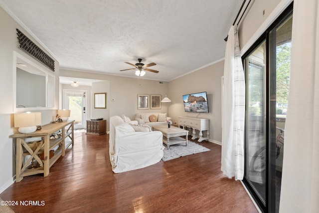 living room with baseboards, a ceiling fan, ornamental molding, dark wood-style flooring, and a textured ceiling