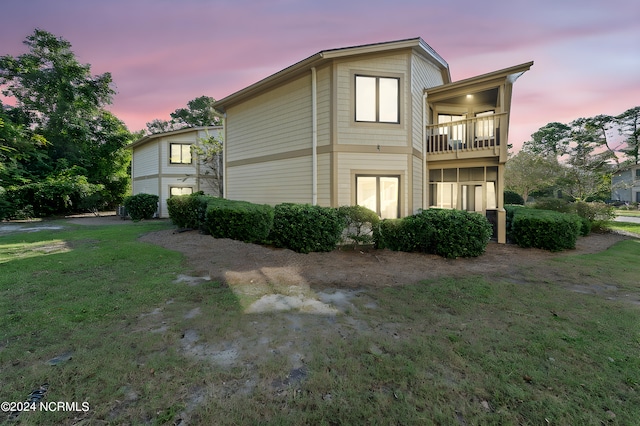 property exterior at dusk with a balcony and a yard