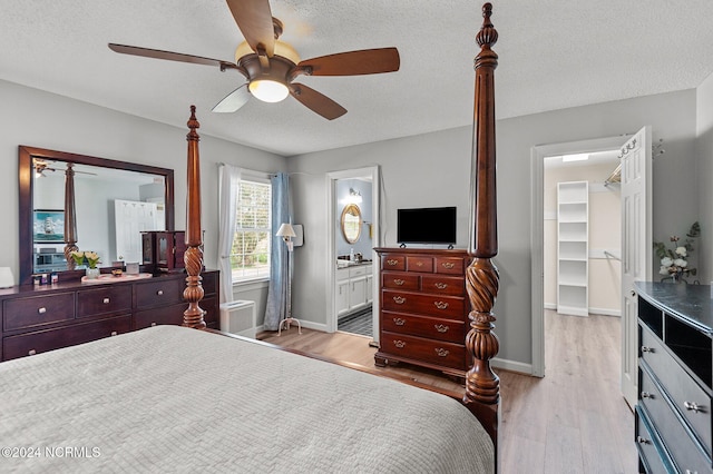 bedroom with light wood-type flooring, a textured ceiling, ceiling fan, a walk in closet, and ensuite bath