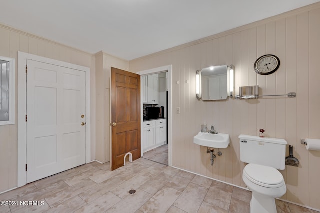 bathroom featuring crown molding, wooden walls, toilet, and sink