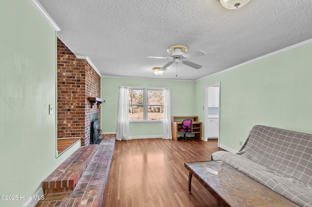 unfurnished room featuring ceiling fan, a brick fireplace, wood-type flooring, a textured ceiling, and ornamental molding