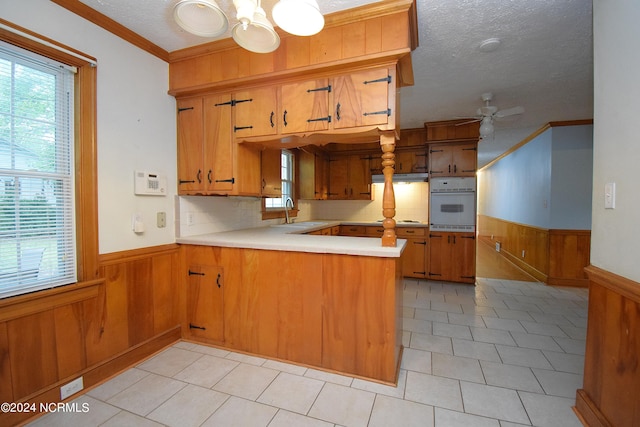 kitchen featuring kitchen peninsula, backsplash, oven, crown molding, and ceiling fan