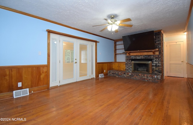 unfurnished living room with ceiling fan, french doors, a brick fireplace, a textured ceiling, and hardwood / wood-style floors