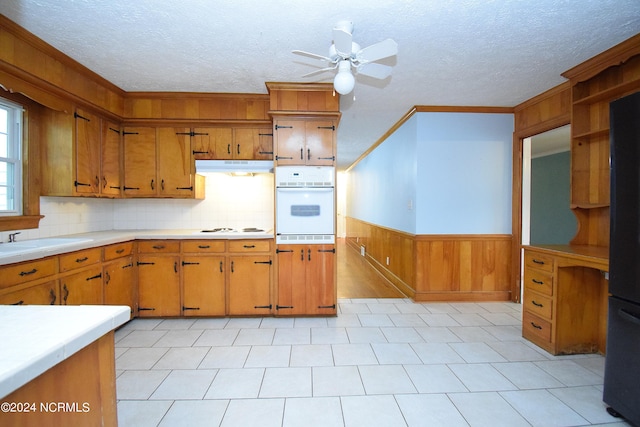 kitchen with backsplash, white appliances, ceiling fan, wooden walls, and sink