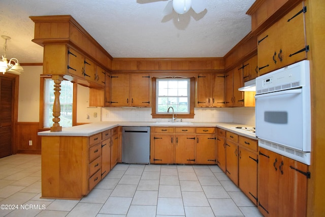 kitchen featuring sink, ceiling fan with notable chandelier, wood walls, decorative backsplash, and white appliances