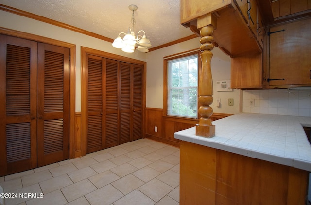 kitchen with a textured ceiling, wooden walls, backsplash, tile countertops, and an inviting chandelier