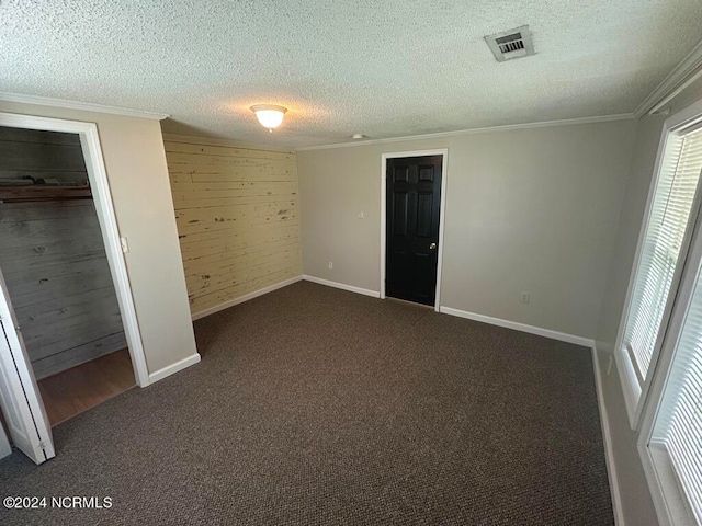 unfurnished bedroom featuring ornamental molding, a textured ceiling, wooden walls, a closet, and dark colored carpet