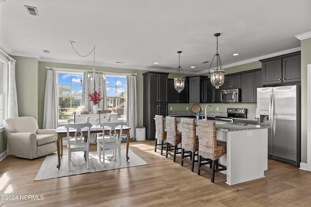 kitchen featuring a kitchen breakfast bar, hardwood / wood-style floors, appliances with stainless steel finishes, and a kitchen island with sink