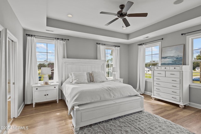 bedroom with ceiling fan, a tray ceiling, and light hardwood / wood-style floors