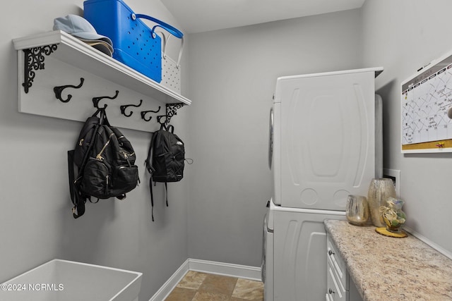 clothes washing area featuring stacked washing maching and dryer and cabinets