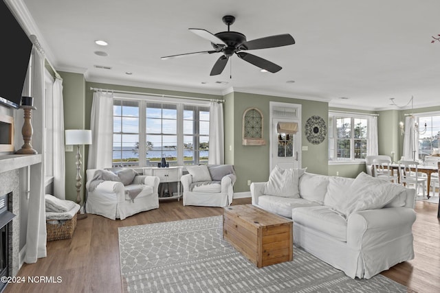 living area with a ceiling fan, wood finished floors, a fireplace, ornamental molding, and visible vents
