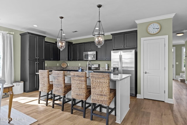 kitchen with an island with sink, ornamental molding, light hardwood / wood-style floors, appliances with stainless steel finishes, and a kitchen bar