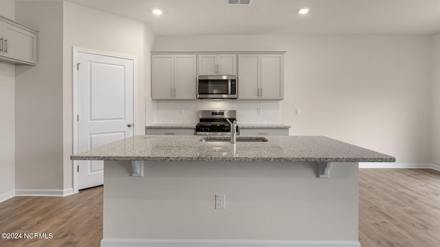 kitchen featuring light wood-type flooring, light stone counters, a center island with sink, and appliances with stainless steel finishes