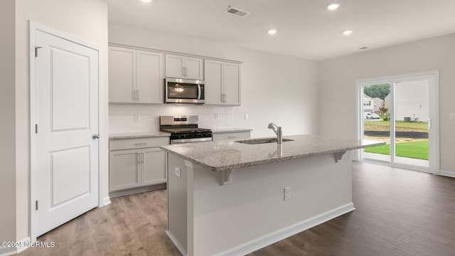 kitchen with light hardwood / wood-style floors, sink, a center island with sink, appliances with stainless steel finishes, and light stone countertops