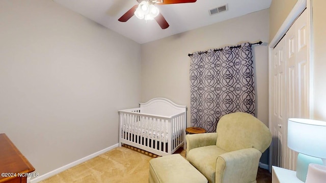 carpeted bedroom featuring a ceiling fan, visible vents, baseboards, a closet, and a nursery area