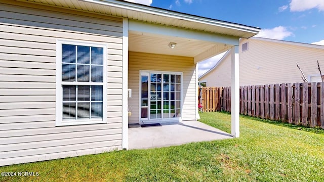 view of exterior entry featuring a patio area, fence, and a lawn