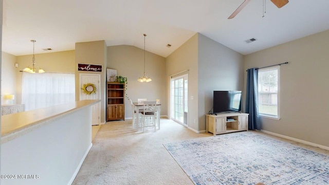 unfurnished living room with light colored carpet, ceiling fan with notable chandelier, visible vents, baseboards, and vaulted ceiling