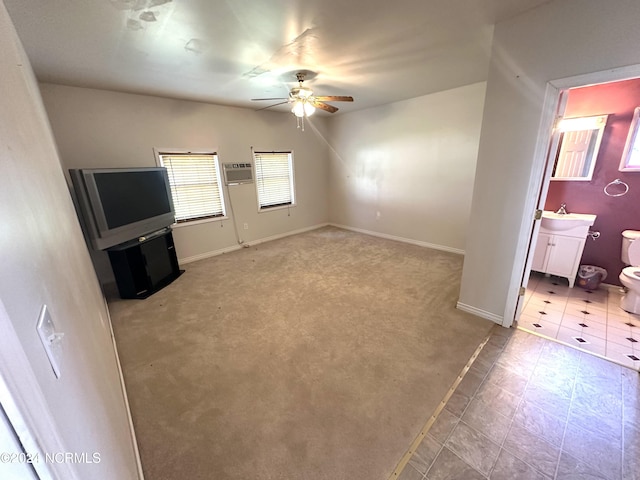 unfurnished living room with an AC wall unit, baseboards, a sink, ceiling fan, and light carpet