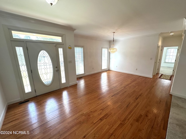 entryway with wood-type flooring, an inviting chandelier, ornamental molding, and a wealth of natural light